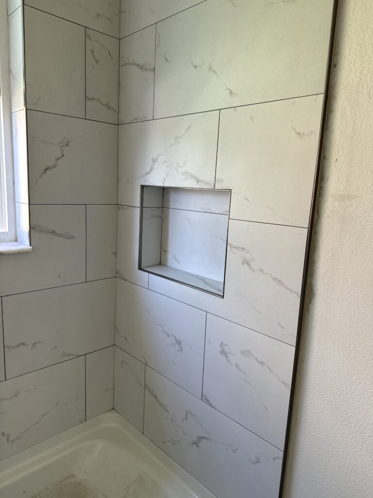 A bathroom with white tile and a window.