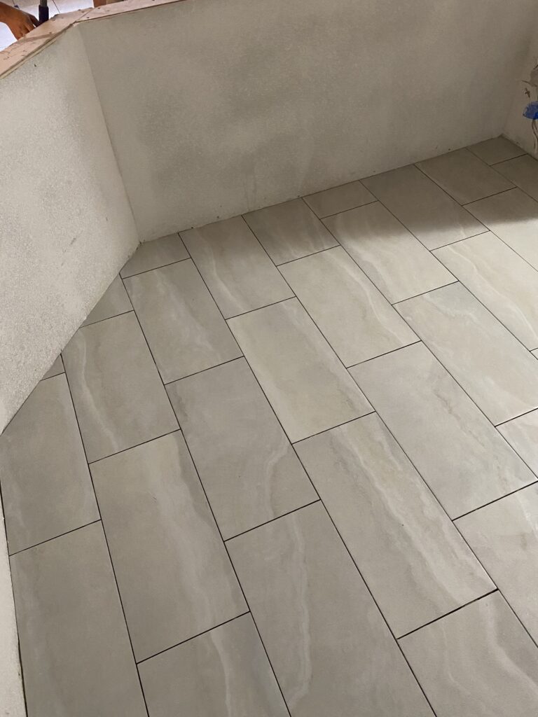 A bathroom floor with white tile and gray grout.